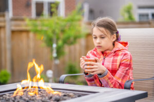 Young Child seated by near tabletop fire pit outdoors, emphasizing safe distance and fire pit injury prevention